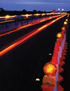 The photo depicts a work zone area at night with the tail lights visible to the left.