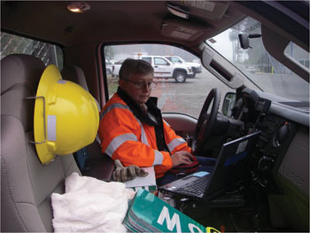Photo. A sign technician uses a laptop while sitting in the cab of a parked maintenance truck.