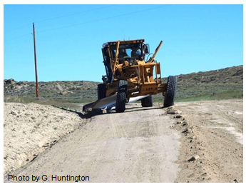 Photo of a motor grader's moldboard shaping the foreslope on a gravel road. Photo by G. Huntington.