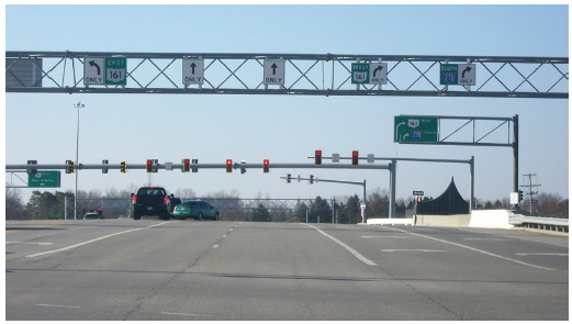 Figure 23. A picture of a five-lane approach to a signalized intersection at which an advance mast arm has been installed that displays lane-use control signs.  Above the left lane is a left-turn-only Mandatory Movement Lane Control (R3-5) sign and a white-on-green guide sign for East Ohio Highway 161.  Above the next two lanes are through-only Mandatory Movement Lane Control (R3-5a) signs.  Above the two lanes on the right are right-turn-only Mandatory Movement Lane Control (R3-5R) signs; above the rightmost lane is also a white-on-green guide sign for South Interstate 270 and above the adjacent lane is a white-on-green guide sign for West Ohio Highway 161.