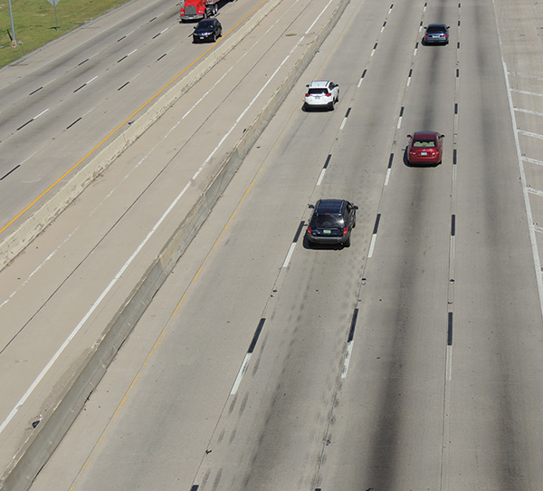 Figure 57. A picture of a section of eight-lane freeway with concrete surface on which the traditional white broken lane lines are supplemented by black broken lane lines.  The black lines are immediately downstream of the white lines to provide contrast to the white markings.