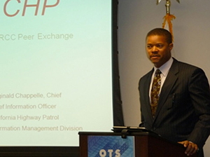 Photograph of Chief Chappelle speaking from behind a podium, next to a presentation screen