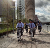 Men in suits riding bicycles near a bay in Tampa, FL.