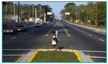 Photo of a school-aged boy walking in a crosswalk divided by a channelized median.