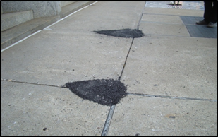 Figure 21 – Description: The areas have been temporarily repaired with asphalt patches. Note the patching material overlaid on the concrete extending beyond the hole.