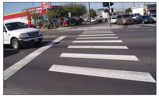 Photo of a series of bright white hash marks across a roadway indicating a pedestrian crosswalk area.