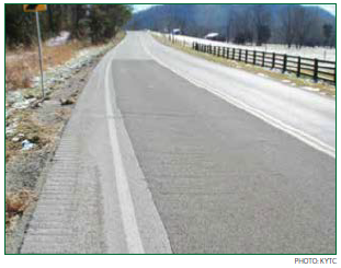 A two-lane rural roadway with darker pavement indicating that the travel lanes have been treated with HFST. Photo: KYTC