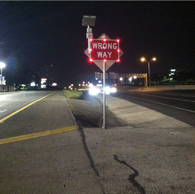 This photo depicts an LED-illuminated Wrong Way sign with a radar detector mounted to the sign. The sign is illuminated by bright red bulbs around the edges.