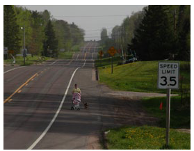 Photo of a woman walking with a stroller on the shoulder of a rural two-lane roadway.