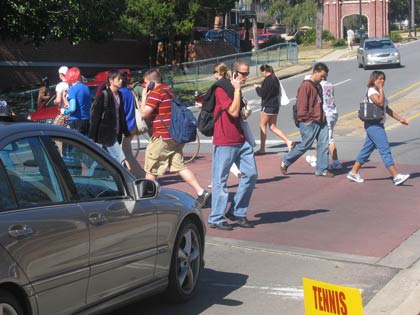 A photo of a car stopped at a crosswalk while students cross the street.