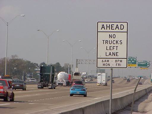 Figure 27. Graphic. Truck lane restriction in Texas. This graphic shows a multi-lane roadway with several vehicles. A static sign off the roadway to the right says 'Ahead, No Trucks Left Lane, 6 a.m.-8 p.m. Mon.-Fri.'