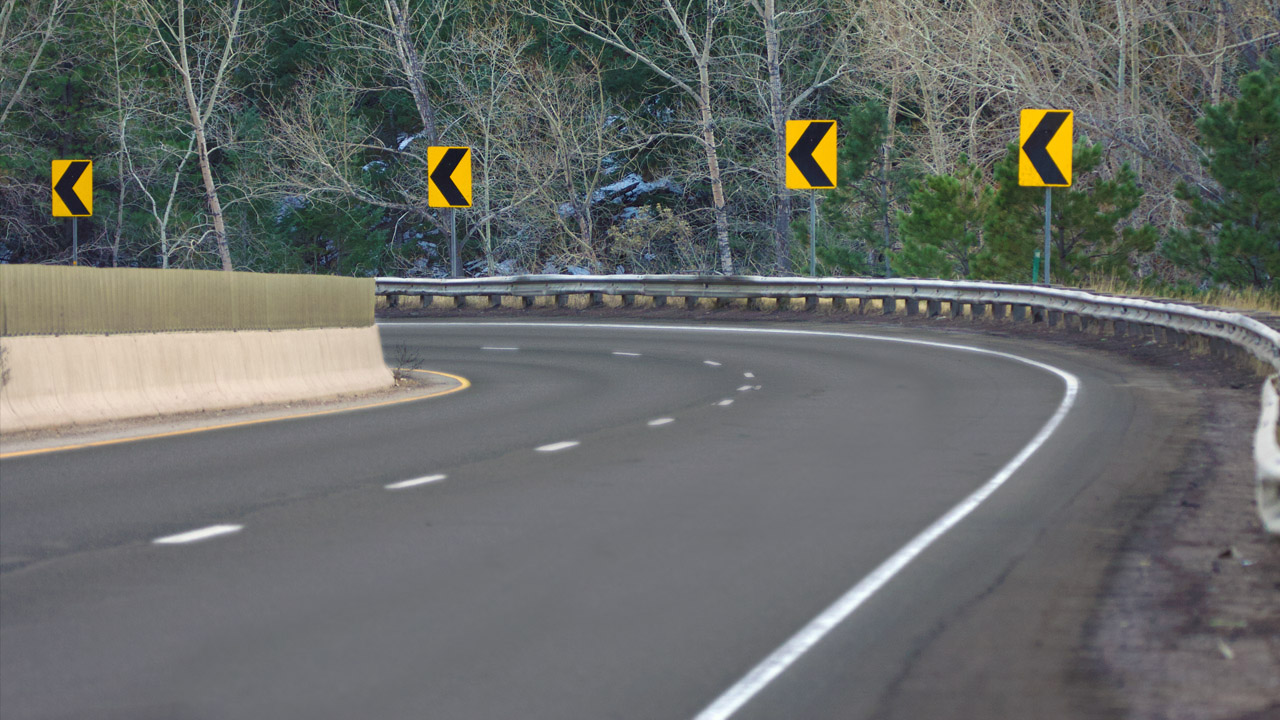 Photo of horizontal curve on a rural road with guard rail and four yellow chevron signs delineating the curve.