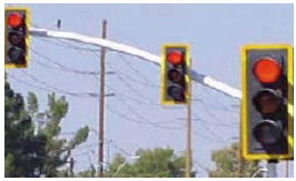 Black traffic signal heads with yellow retroreflective borders on a mast arm during daylight.
