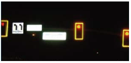 Black traffic signal heads with yellow retroreflective borders on a mast arm during night time.