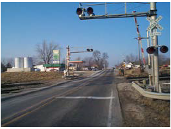 The approach to an at-grade rail crossing featuring gates, bells and flashers.