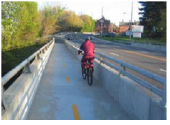 A bicyclist on a dedicated bike lane, protected from traffic by a cement barrier, riding over a bridge.