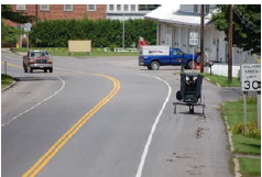 A horse-drawn buggy traveling along a wide shared use shoulder to the right of the roadway.