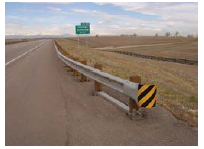 A guardrail separates a wide shoulder from a gentle slope that increases in steepness on the approach to an overpass.