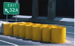 A series of yellow barrels create a crash cushion at the pointed junction of two concrete barriers in advance of a bridge column.