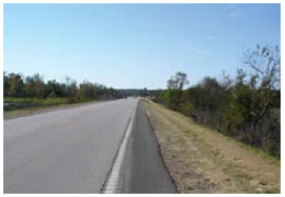 A rural roadway with a wide, relatively flat, clear verge to both right and left of the shoulder.