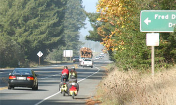 Photo.  Two cyclists riding on a wide shoulder of a two lane road.