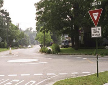 Photo. A rural mini-roundabout. The roundabout consists has one travel lane and a flush concrete circle in the center.