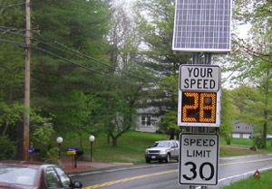 Photo. A solar-powered speed feedback sign. The bottom part of the sign is a typical speed limit sign with a speed limit of 30 MPH. Above that is a changeable display that states 'Your speed 28 MPH' The speed changed based on how fast a vehicle is traveling. Above that is a solar panel to power the sign.