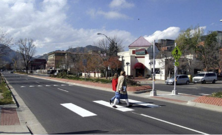 Photo. A crosswalk with a island or median in the center providing a refuge for pedestrians and a shorter distance to cross.
