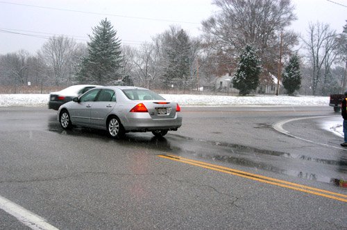 Photo. This photo shows a car on a wet roadway with water clearly ponding in wheel ruts in the pavement behind it.