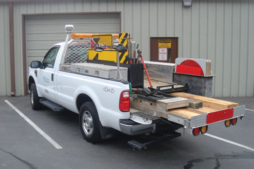 Photo. A truck equipped with flashers and carrying signs, sign posts, parts, and tools is shown.