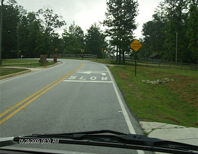 Figure 4: Photo. This photo shows a view of CURVE AHEAD pavement markings and signage from a car. The pavement marking is the word SLOW and a curve arrow preceding the curve. The sign is a yellow diamond that says CURVE AHEAD.