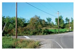 Photo of a T intersection in a rural area with a brightly painted, easily visible stop bar on the stop approach.