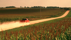 This is a photo of a pick-up truck driving down a dirt rural road.