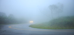 This is a photo of a car driving on a rural road in the fog.