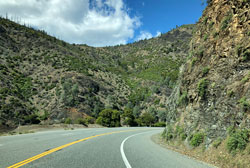 This is a photo of two-lane rural road with a double center line. The road runs through a mountainous area.