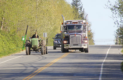 This is a photo of a truck and car passing someone driving farm equipment.