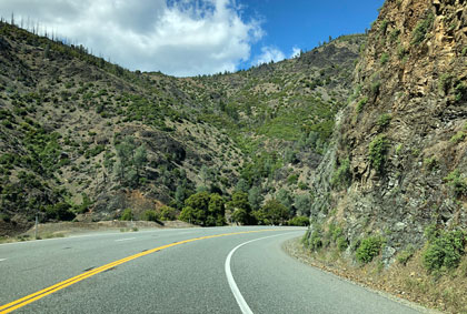 This is a photo of a two-lane rural road with a double center line. The road runs through a mountainous area.