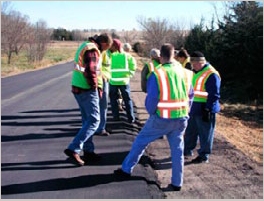 Photo of a group of peers examining a newly installed Safety Edge on a freshly paved rural roadway.