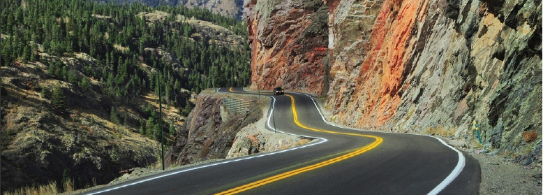 Photo of a vehicle traveling on a winding road through mountainous terrain.