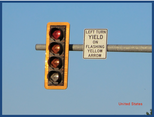Photo of a signal head mounted on a mast arm over a roadway. The signal head features a retroreflective backplate that surrounsds the signal head, improving its visibility at night. A sign next to the signal head reads 'Left turn yield on flashing yellow arrow.'