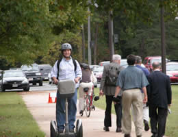 Front view of a Segway rider shares the roadway with pedestrians and a bicyclist.