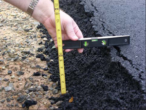 Photo. BEFORE - In a typical pavement resurfacing project, the asphalt at the edge remains soft because there is no compaction. Repeated vehicle impacts and erosion combined with asphalt cracking gradually create a vertical edge that can be hazardous to drivers.