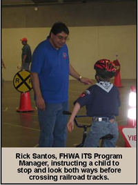 Rick Santos, FHWA ITS Program Manager, instructing a child to stop and look both ways before crossing railroad tracks.