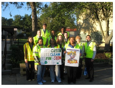 Group of adults wearing retroreflective vests and displaying signs encouraging walking to school.