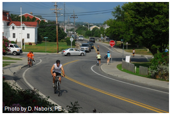 Photo of a busy stop-controlled intersection in a Rhode Island suburb where there is vehicle, pedestrian, and bicycle traffic. Photo by D. Nabors.