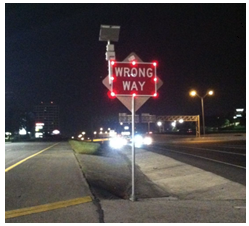This photo depicts an LED-illuminated Wrong Way sign with a radar detector mounted to the sign. The sign is illuminated by bright red bulbs around the edges.