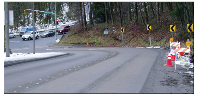 Freshly laid asphalt features both a steep grade and a sharp curve on the approach to an intersection.