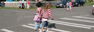 Two children crossing holding hands while crossing the street in a crosswalk.