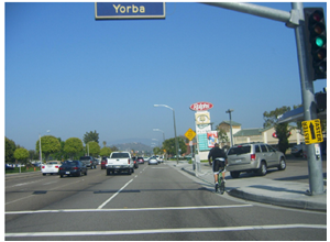 A bicyclist hugs the curb on a multilane road without bicycle lanes or other facilities.