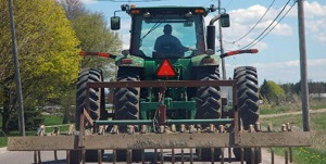 Photo shows a wide tractor with farm equipment attached to the back.